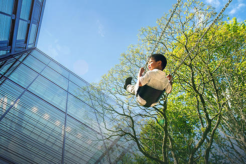 Child on swing under a tree next to a glass building
