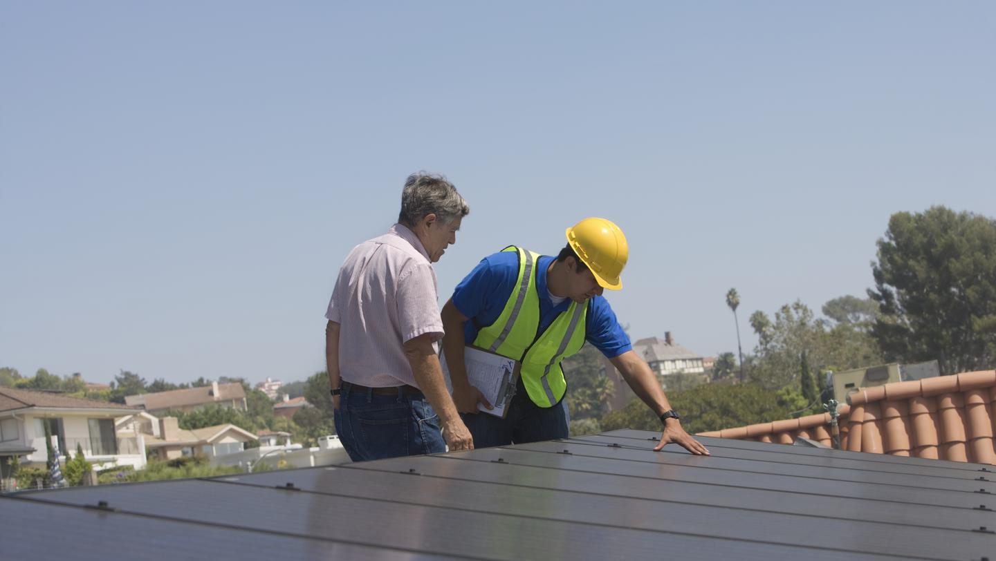 Maintenance workers stand with solar array on rooftop in Los Angeles, California