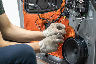 A technician works on the audio wiring for speakers inside a car door panel