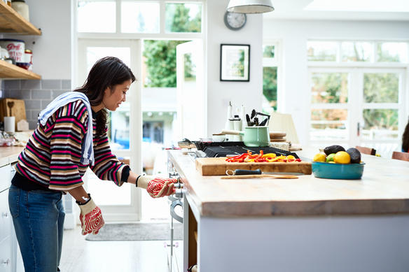 Woman adjusting oven and preparing dinner in kitchen