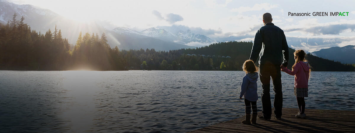A father stands on a dock in a lake, staring at the mountains and pine trees with his children