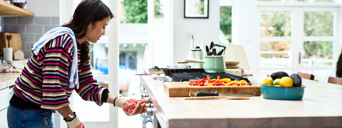 Woman adjusting oven and preparing dinner in kitchen